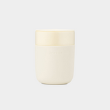 Cream ceramic travel mug with matte silicone sleeve and splash-resistant lid