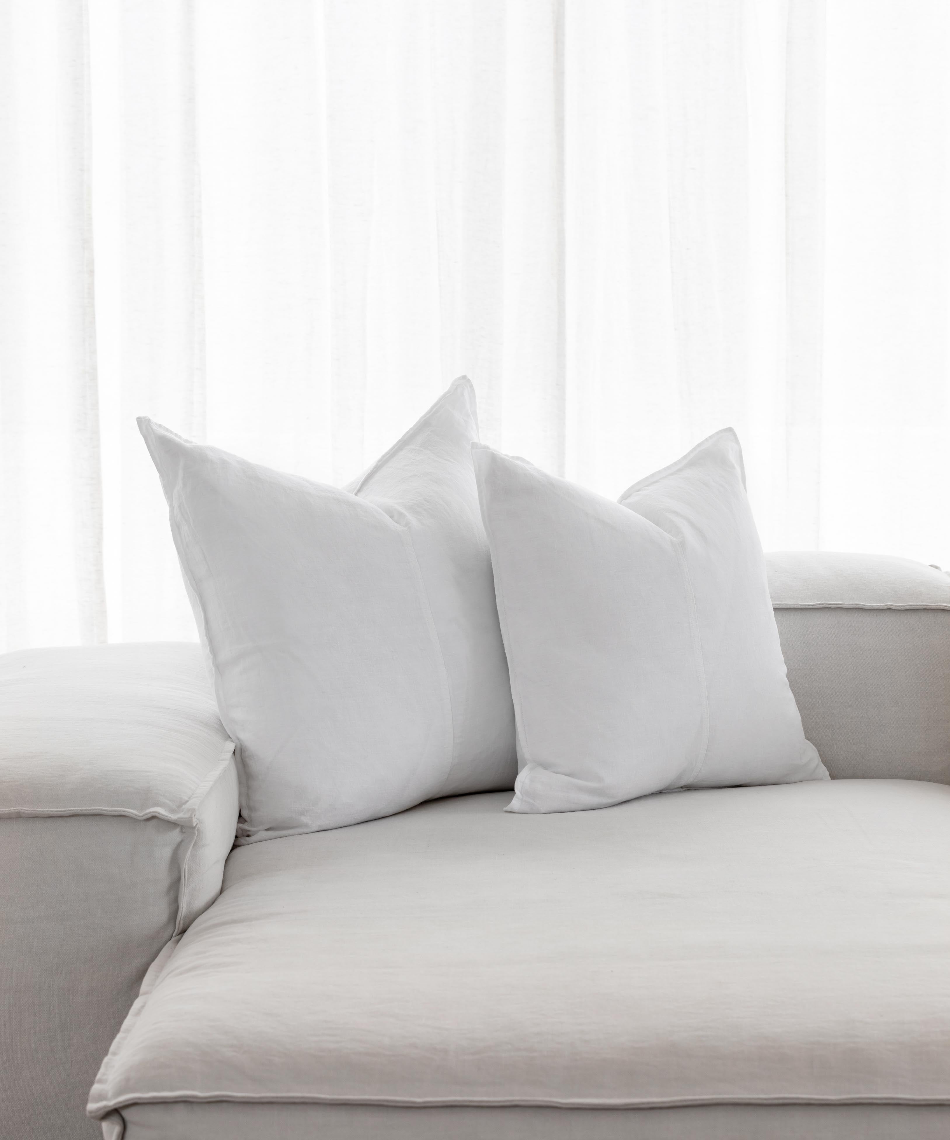 White linen throw cushions with flanged edges and vertical stitching on a light sofa