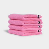 Stack of four soft bubblegum pink face washer towels neatly folded for spa-like skincare routine