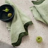 Sage and forest green linen table napkin set with waved edges on a textured surface