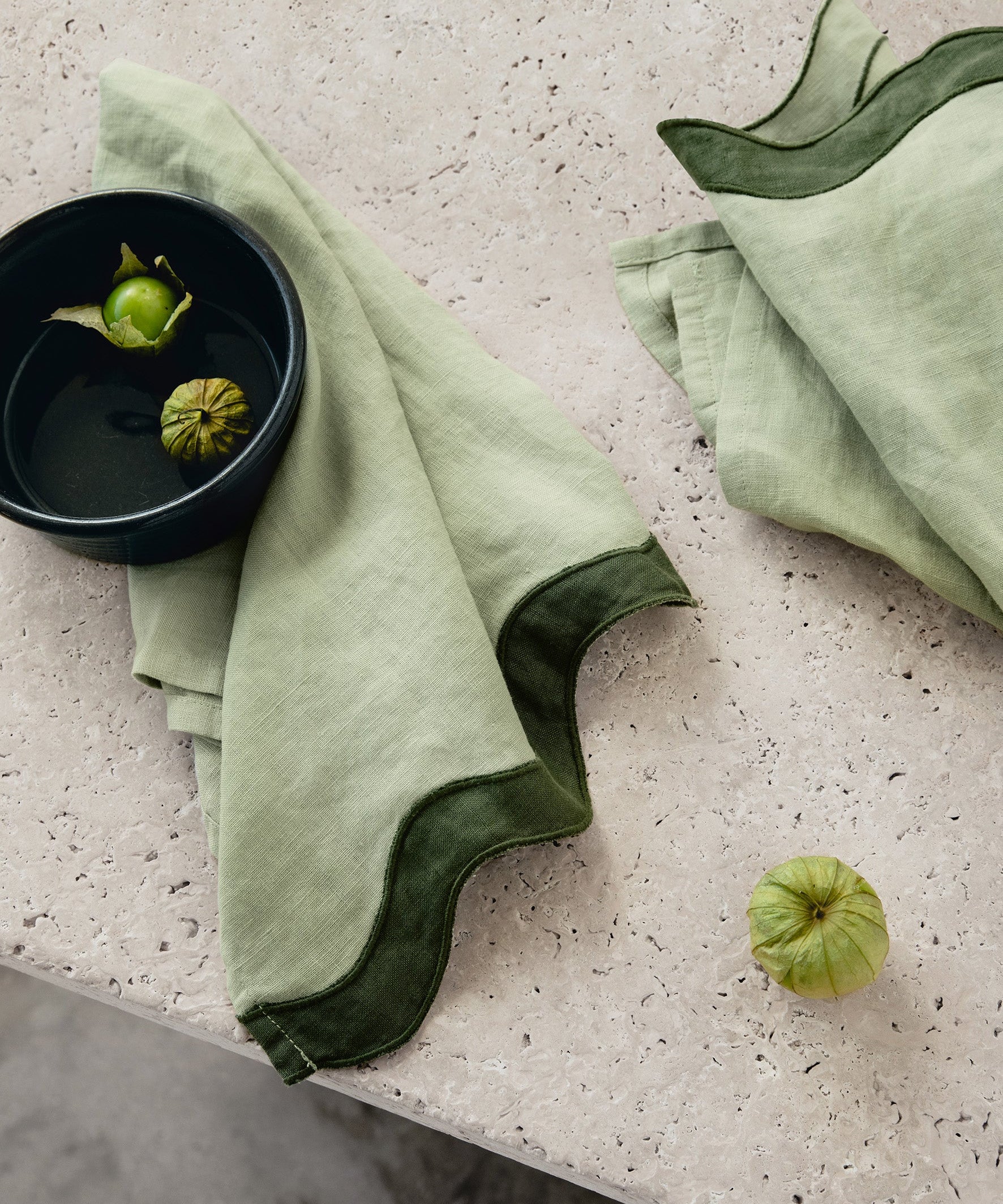 Sage and forest green linen table napkin set with waved edges on a textured surface