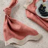 Rose pink and beige waved linen table napkin set on a textured surface with a small dish of grapes