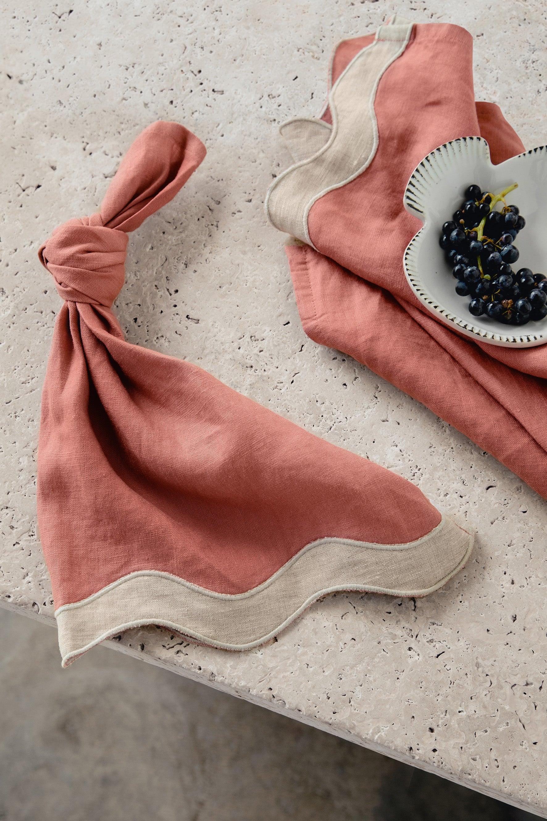 Rose pink and beige waved linen table napkin set on a textured surface with a small dish of grapes