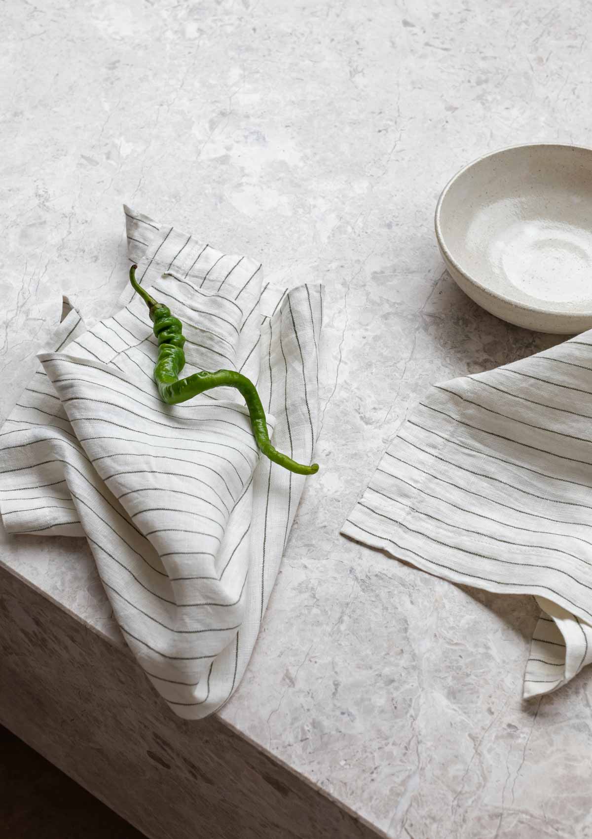 Striped olive linen table napkin set made from 100% European flax with fine hem finish on marble surface