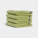 Stack of four green face washer towels neatly folded with a white background