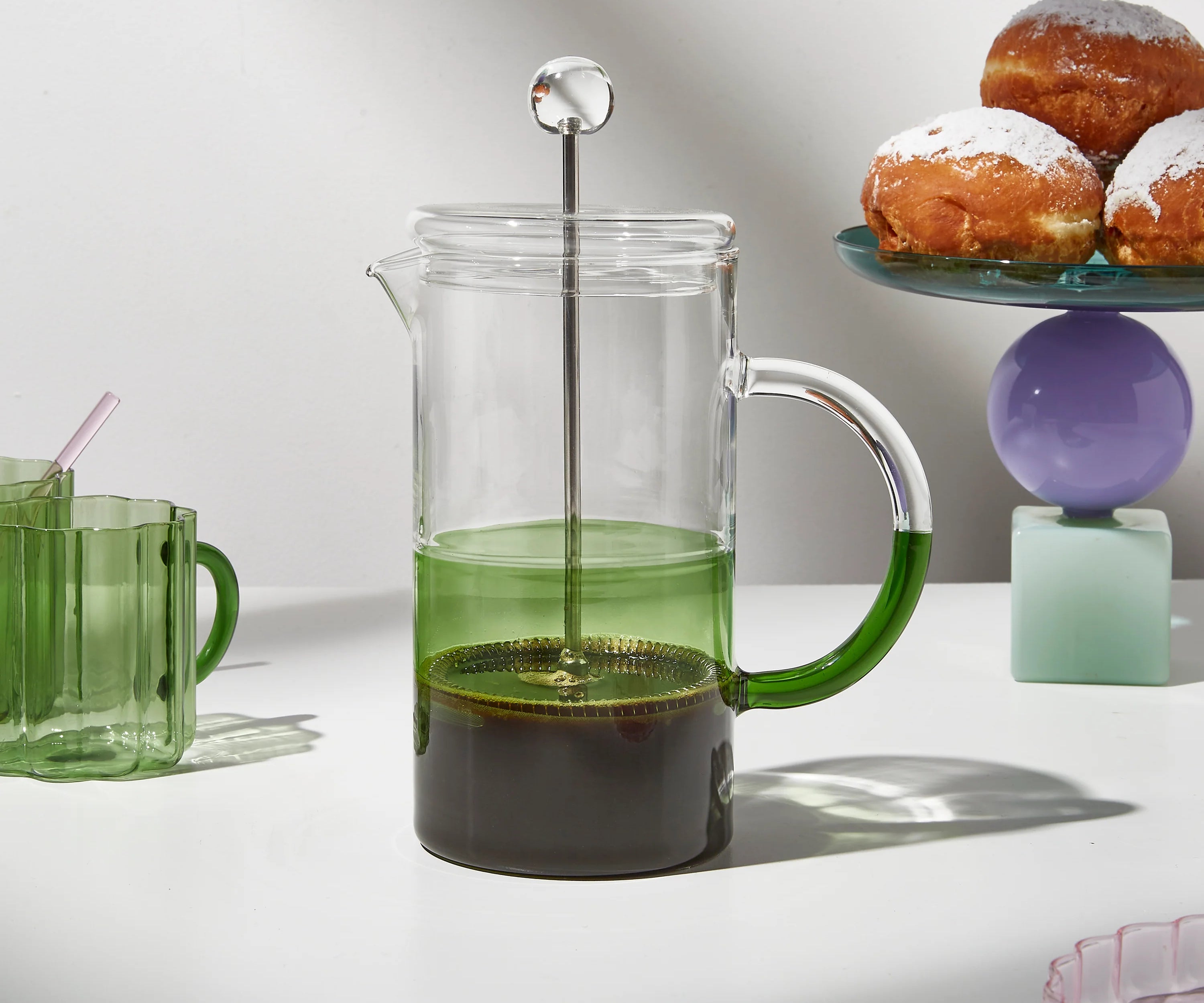 green coffee plunger on a lifestyle shot with muffins in back