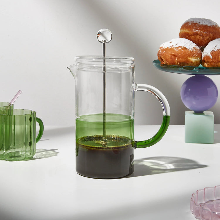 green coffee plunger on a lifestyle shot with muffins in back