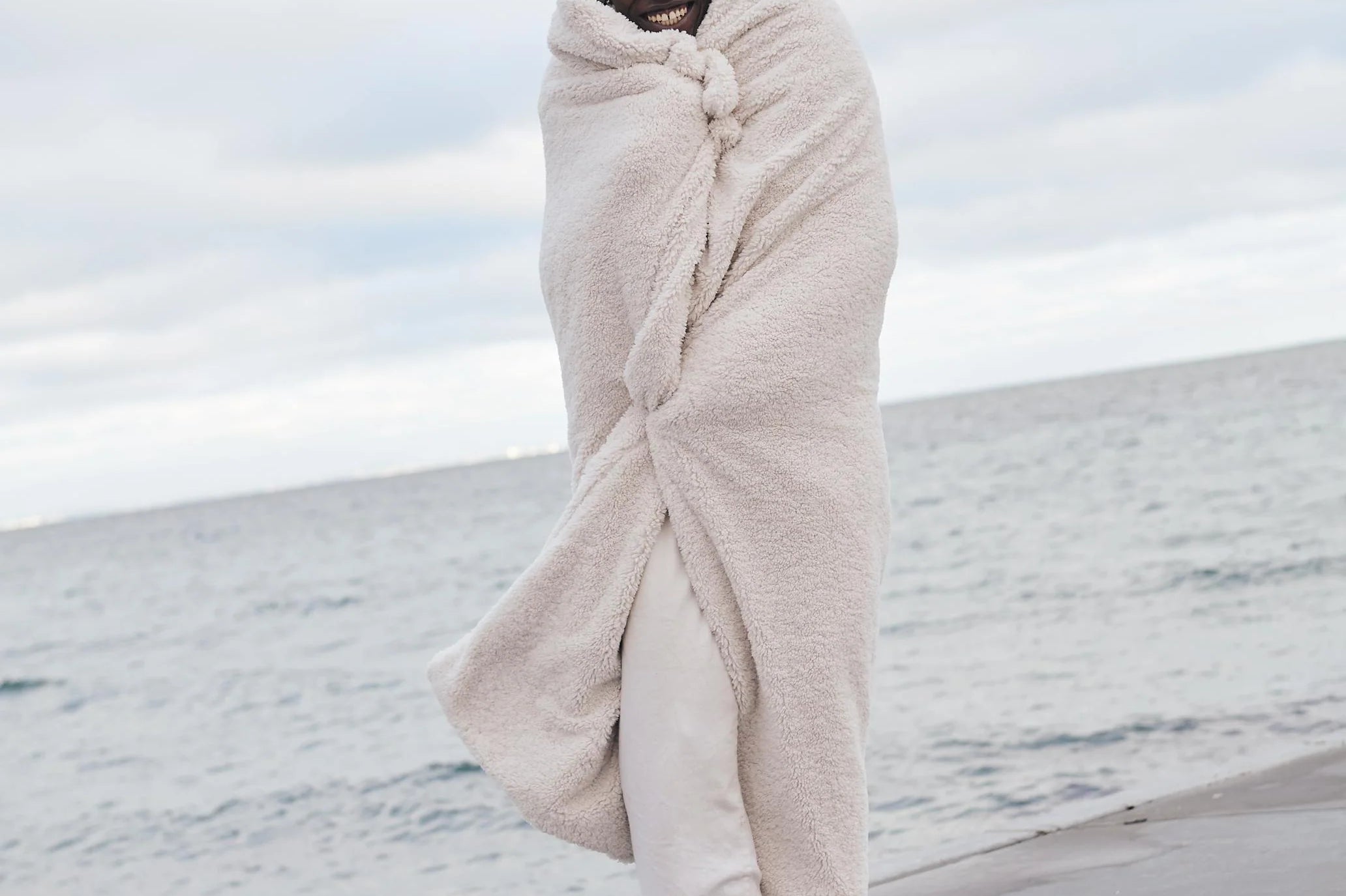 guy standing on beach with white throw blanket over him