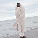 guy standing on beach with white throw blanket over him