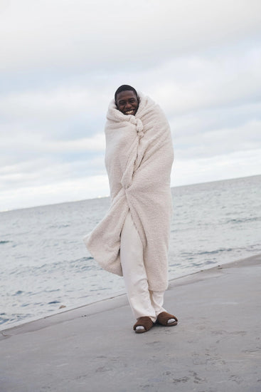 guy standing on beach with white throw blanket over him