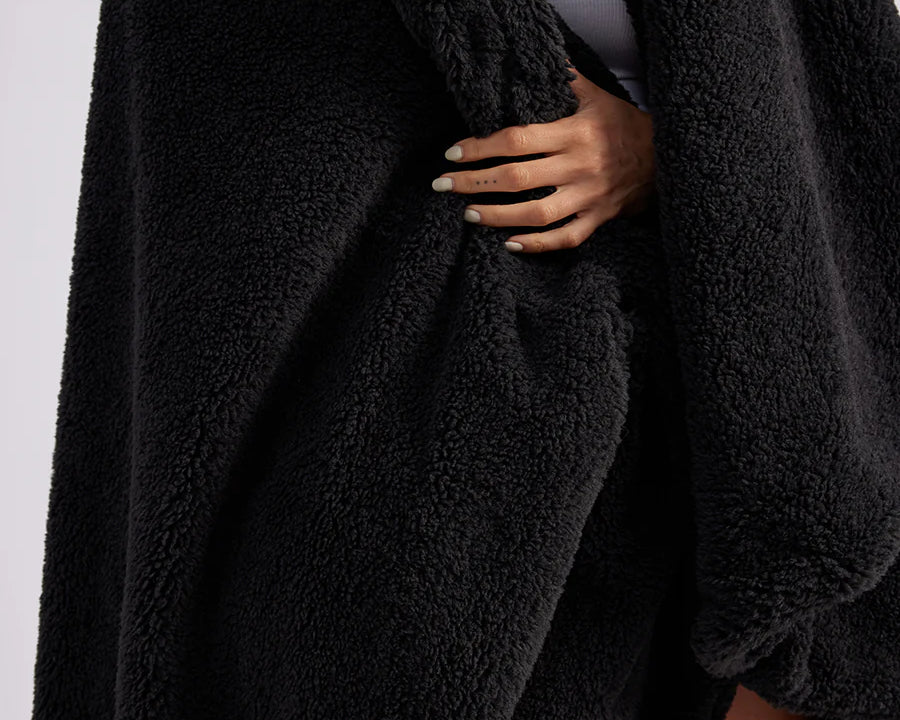 up close shot of woman standing with black fluffy throw blanket around her