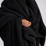 up close shot of woman standing with black fluffy throw blanket around her