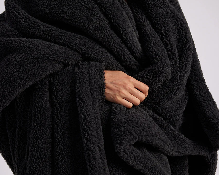 up close shot of woman standing with black fluffy throw blanket around her
