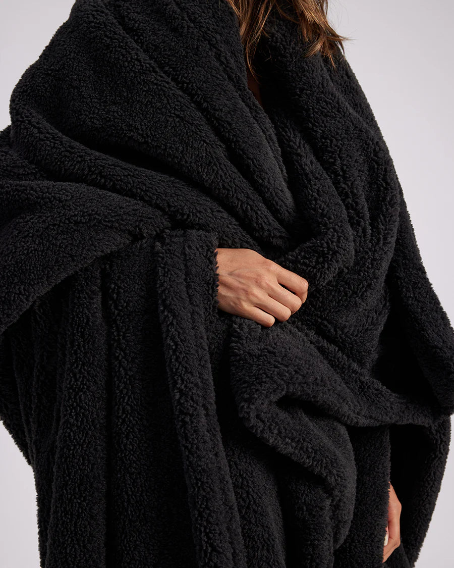 up close shot of woman standing with black fluffy throw blanket around her