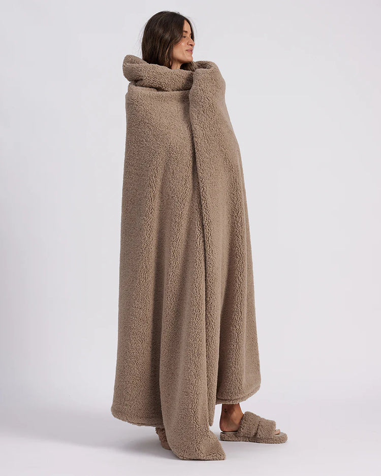 girl wrapped up with a beige throw blanket standing