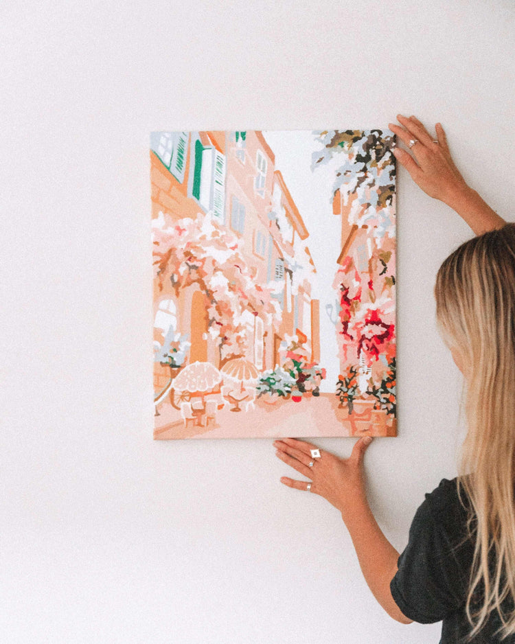 woman hanging up wall art of a Parisian street