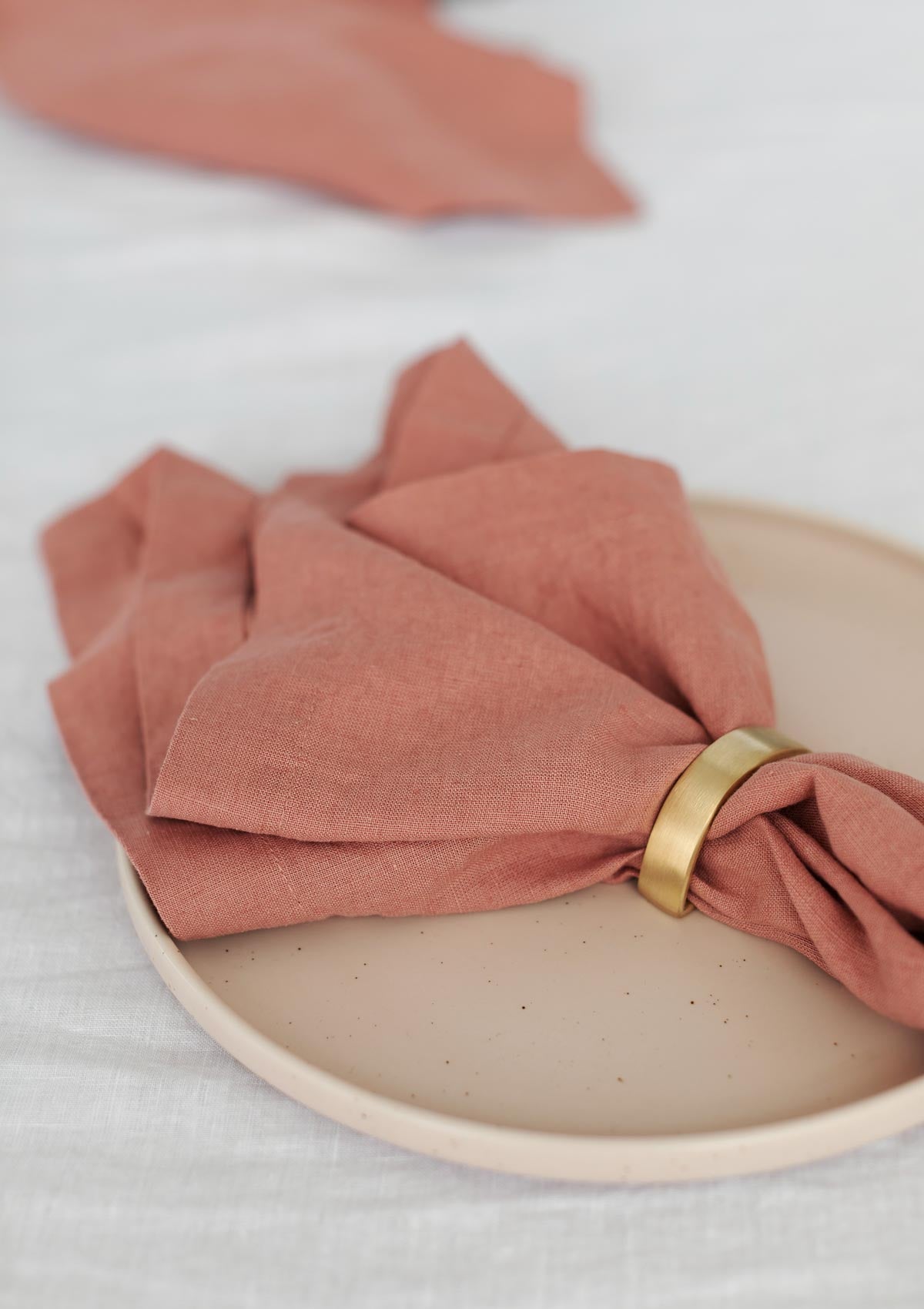 rose pink napkin with a gold napkin ring around it 