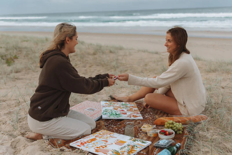 two girls sitting on beach painting paint by number kits