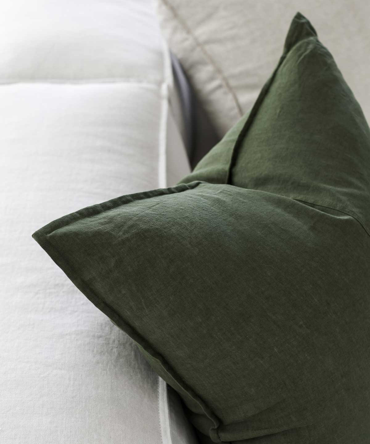up close image of a forest green linen cushion sitting on a couch 